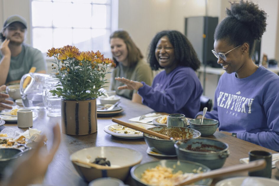 People sitting at table laughing with bowls of food made out of clay on the table