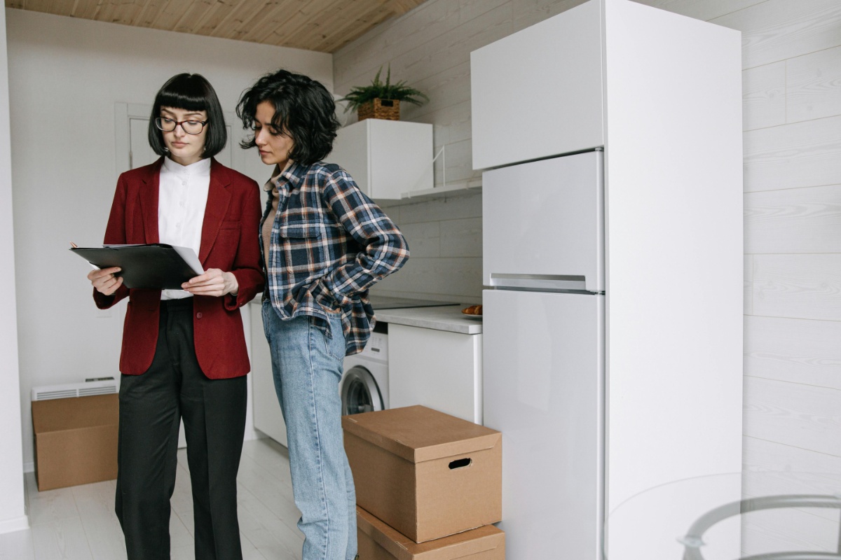 Two women stand in a kitchen, comparing and discussing appraisal documents vs. inspection reports for a home.