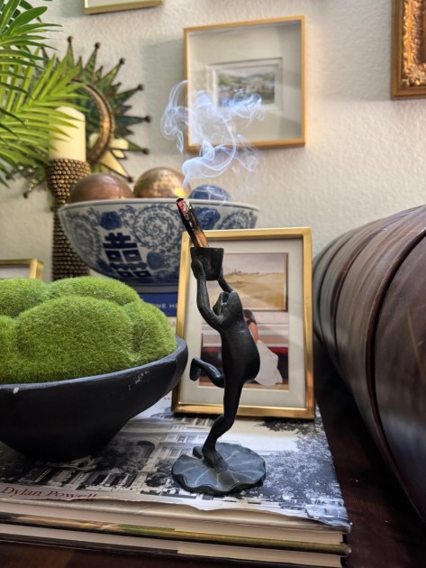 A dancing frog statuette holding a lit piece of palo santo wood, an example of animalcore design from Rachel Jackson.