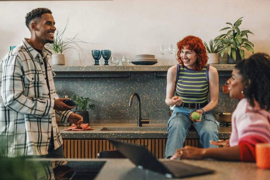 Three students sit around their rental apartment chatting. When considering between living on campus vs. off campus, they decided to rent an apartment off campus together.