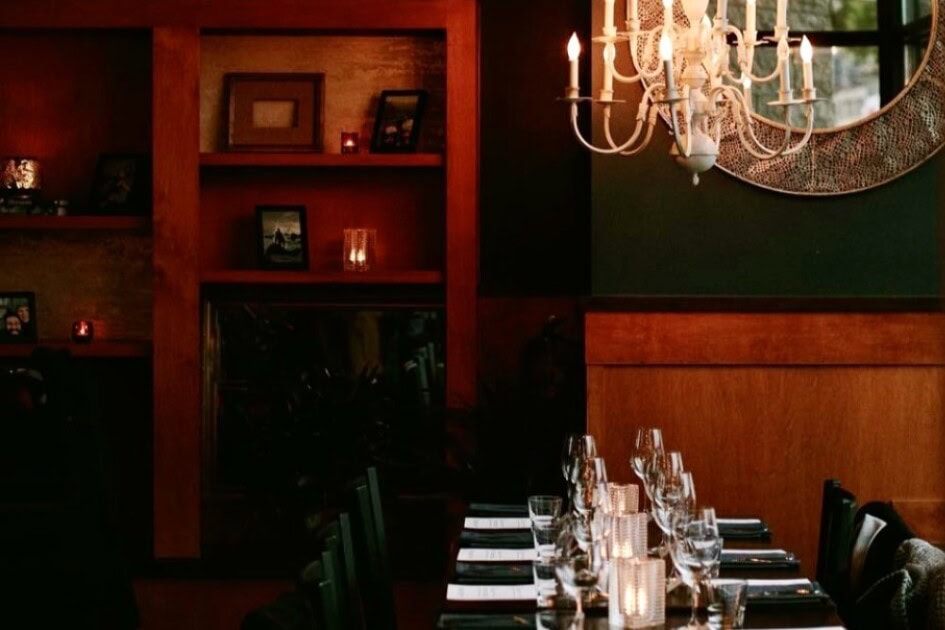 a long table with wine glasses sits below a chandelier at the dim lit vibey SWeL Restaurant in Fremont, Seattle