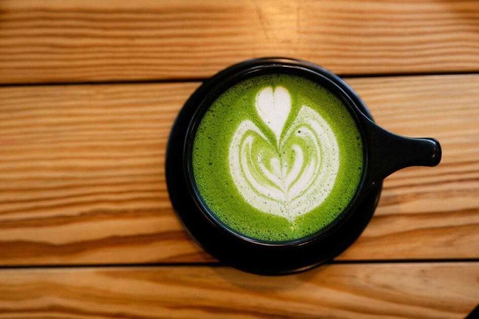 A cup of hot matcha with latte art in a heart