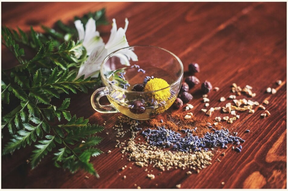 A mug of loose leaf tea with flowers and spices next to it