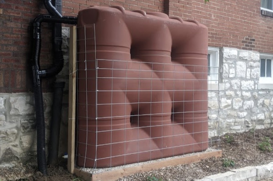 a custom terracotta rainwater harvesting system sits outside a similarly colored red brick home