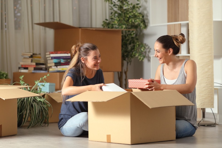Two friends unpack a moving box in the new house they bought. 