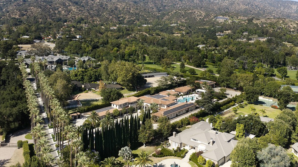 High-altitude aerial photograph of an expansive luxury estate set within a private, tree-lined valley surrounded by hills.