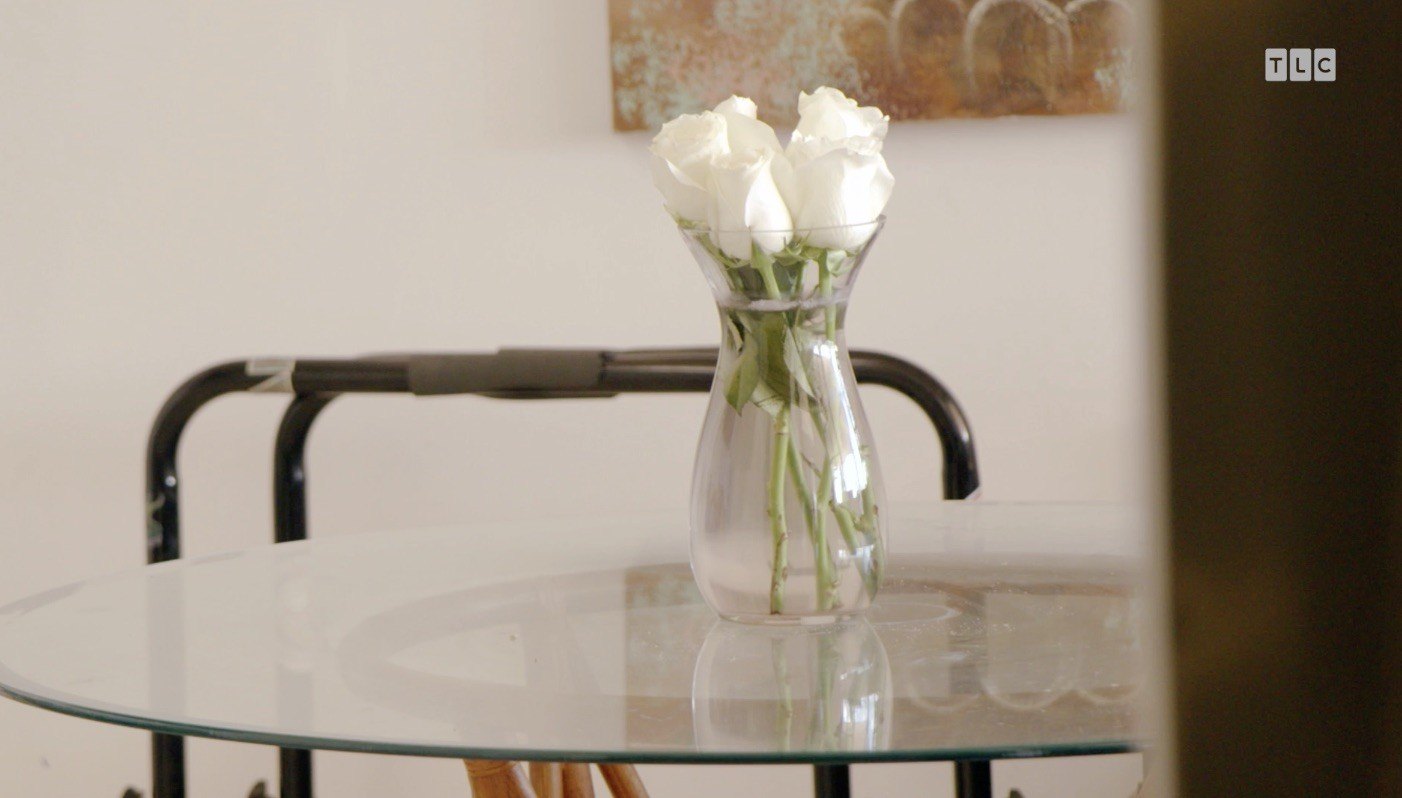 The trio pass by a glass table with a vase of white roses on top in the entryway.