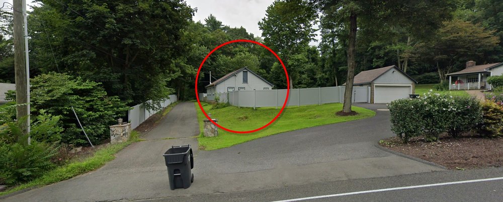 49 Putnam Rd, Bethel, Connecticut 06801 Gray suburban residence featuring a detached garage and barn for apartment complex, expansive asphalt driveway, and private fenced-in yard surrounded by lush greenery