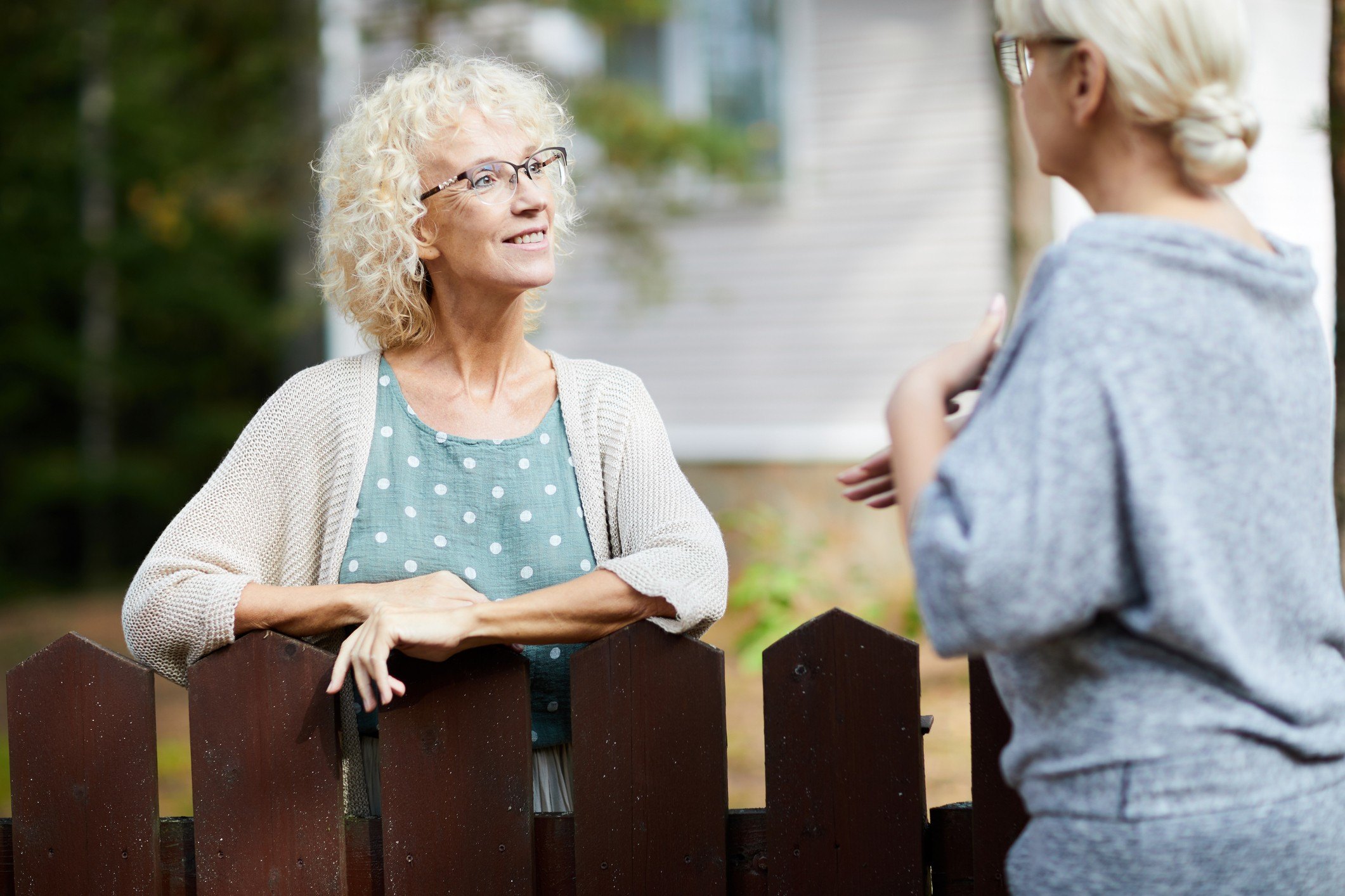 Two mature female neighbours talking through fence