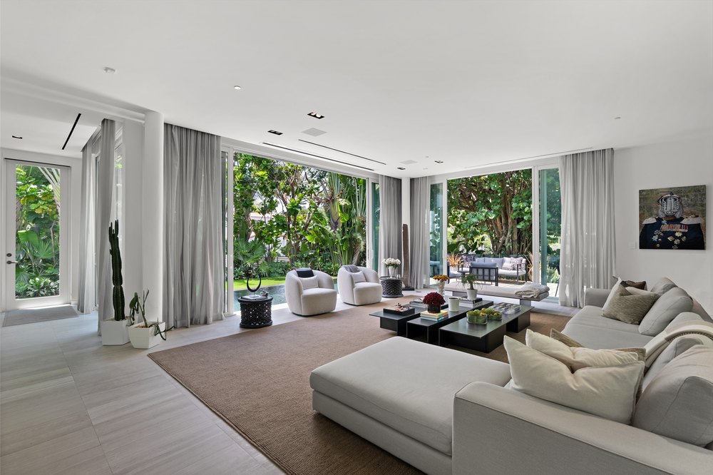 Bright living room space with neutral-toned furniture and large sliding glass walls that open directly onto a private pool area.