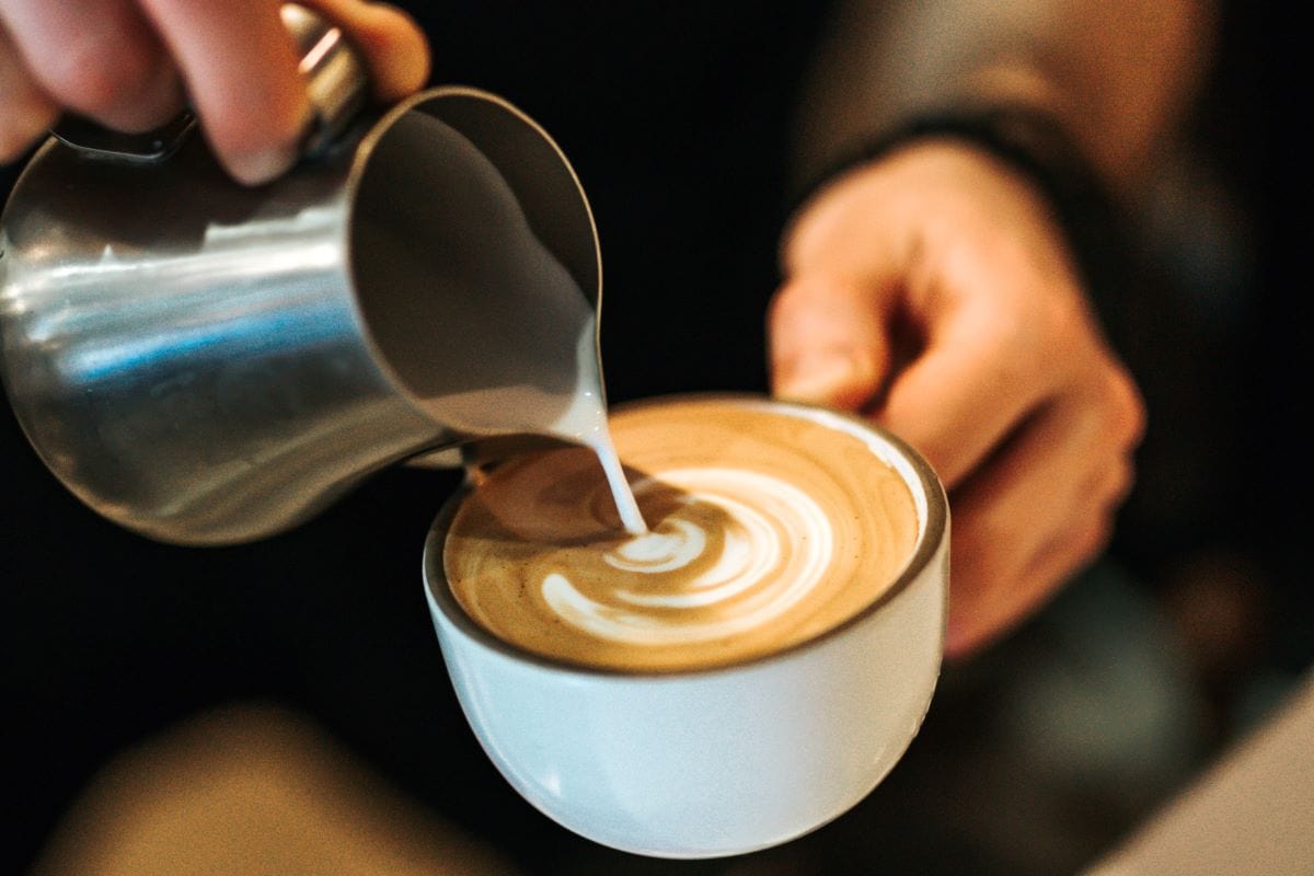 person pouring cream into a coffee cup