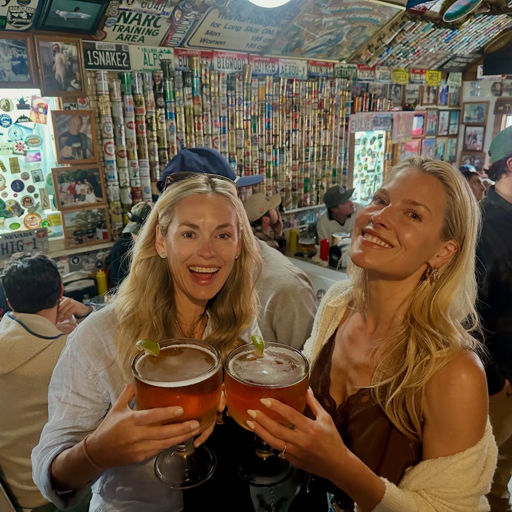 Two Women Toasting with Large Drinks in a Rustic Bar