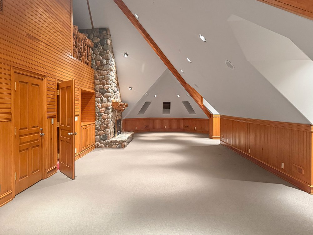 Spacious Upper-Level Vaulted Room with Stone Fireplace, Wood Panel Accent Walls, and Carpet