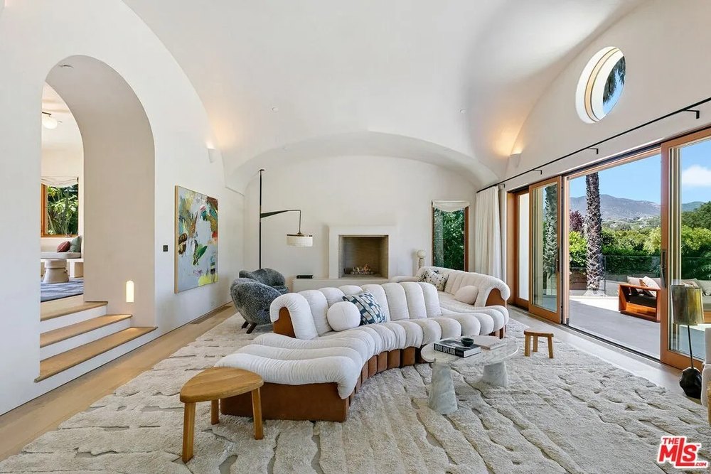 large, white curved sofa sits on a textured rug in a room with a vaulted ceiling and an arched entryway.