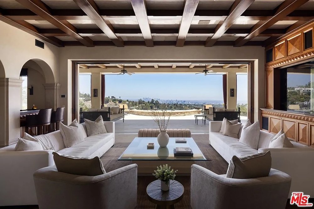 Sophisticated open-concept living room featuring exposed wood beams and seamless indoor-outdoor access to city vistas.