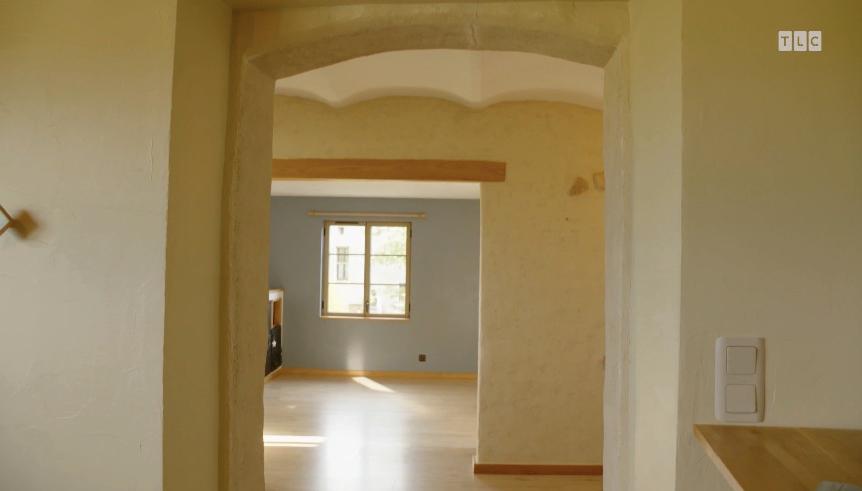 Cream walls with a yellow tint run throughout the residence, as do various warm wooden accents, such as thin floor baseboards, ceiling beams, and accent pieces above door openings.