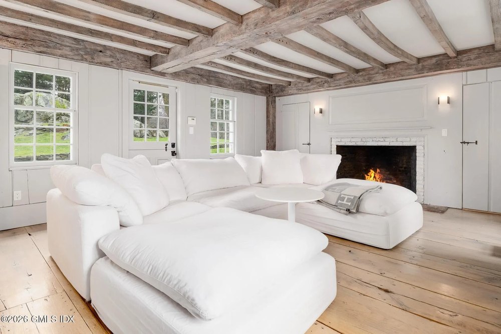 A fluffy white couch with an Hermes blanket in front of a fireplace in Chris Simms equestrian estate in Greenwich Connecticut