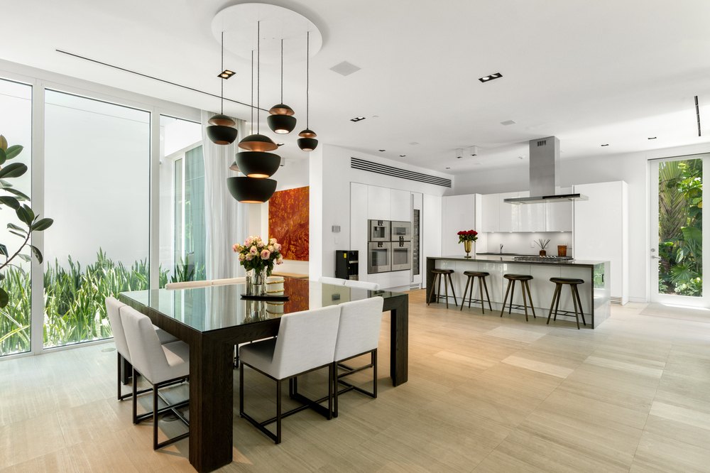 Open-concept dining room with a dark wooden table and white chairs located next to a modern kitchen with a large island.