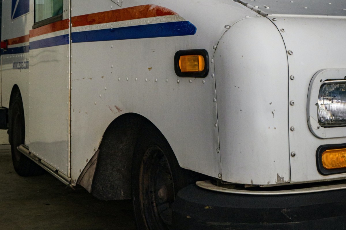 postal delivery truck delivering mail to an apartment address