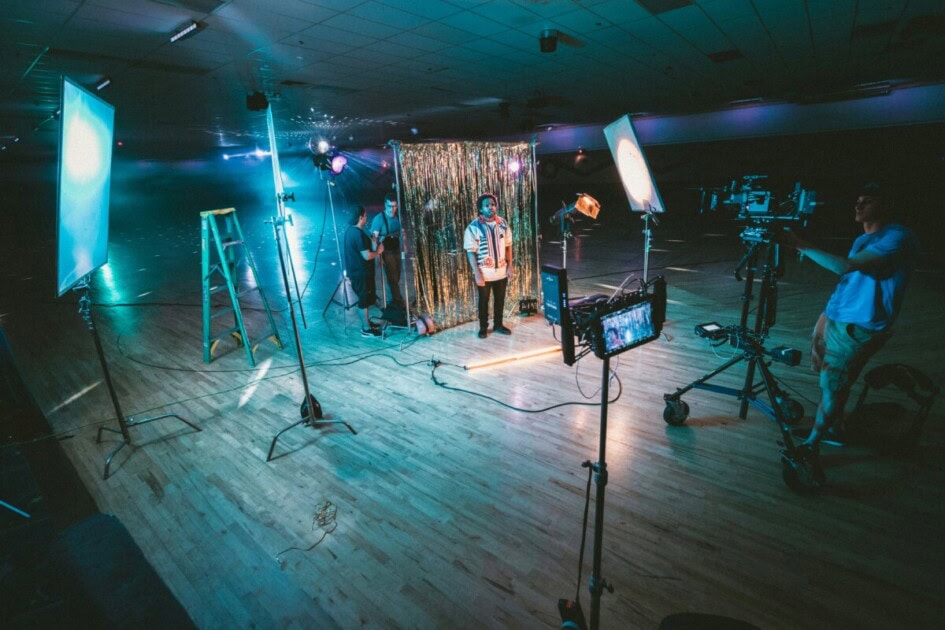 A man stands in front of a camera with film lighting.