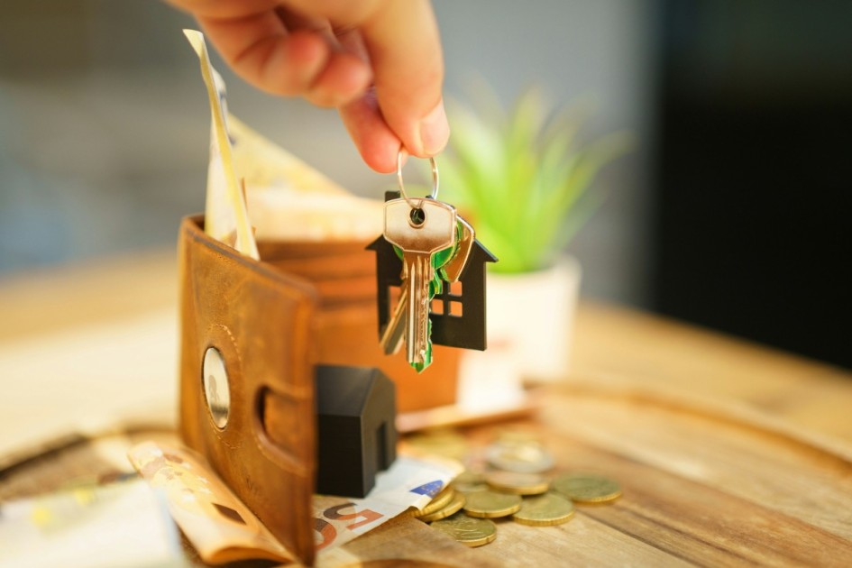 a wallet with money sits behind a hand holding a set of house keys
