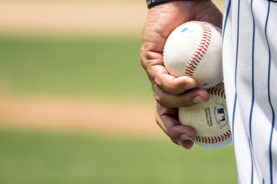 A pitcher holds two baseballs in his hand