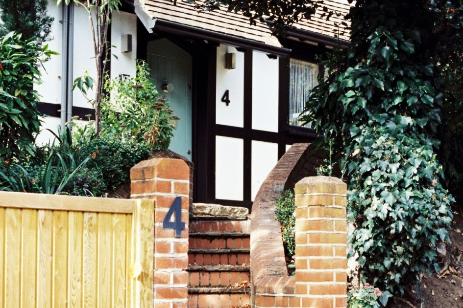 a black and white house with brick stairs and lush greenery has a home numerology of 4 as seen on the home's outside and on a brick pillar near the stairs