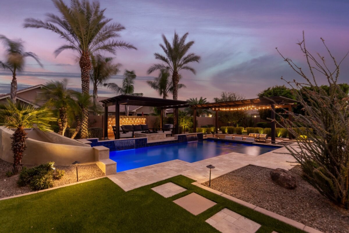 luxurious backyard pool with palm trees and bar lit up at night