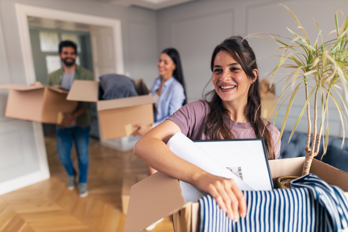 A young woman moves boxed into a house followed by two other people helping her move into a family member's house.