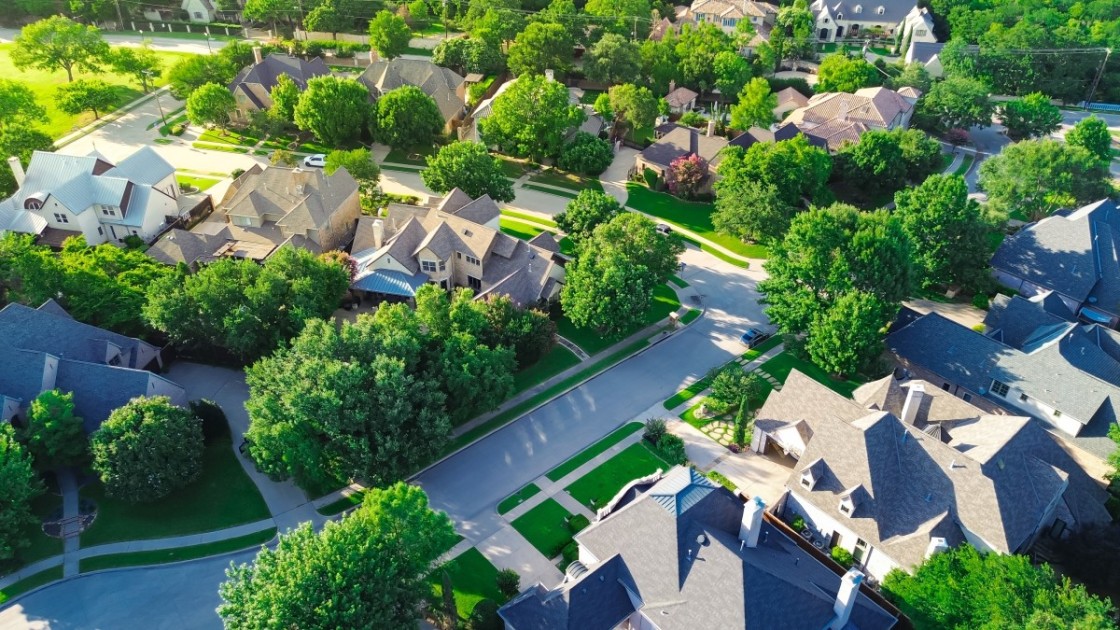 An aerial view of a neighborhood street with lots of bushy green trees.