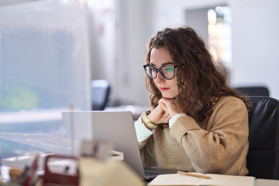 A girl with curly hair and glasses looks online at homes to buy out of state. 