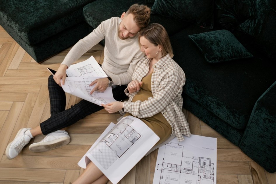 a couple sits on the floor next to a large sectional couch looking at various floorplans of new construction homes