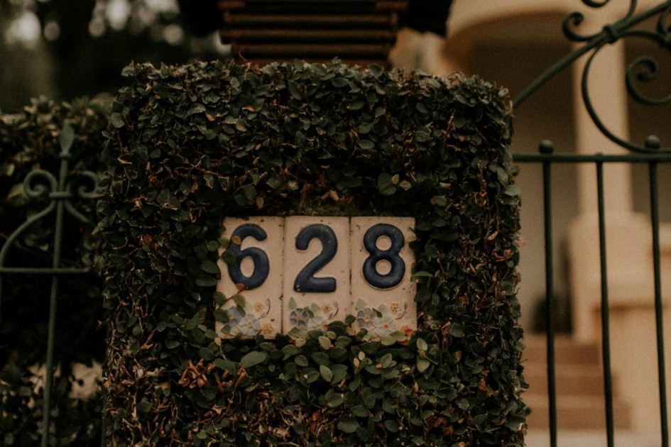 a tile sign reading "628" sits in greenery on a gate outside a home