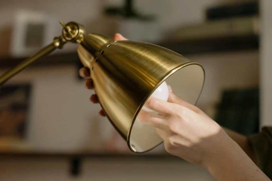 two hands screw a lightbulb into a brass lamp representing home electricity utility charges