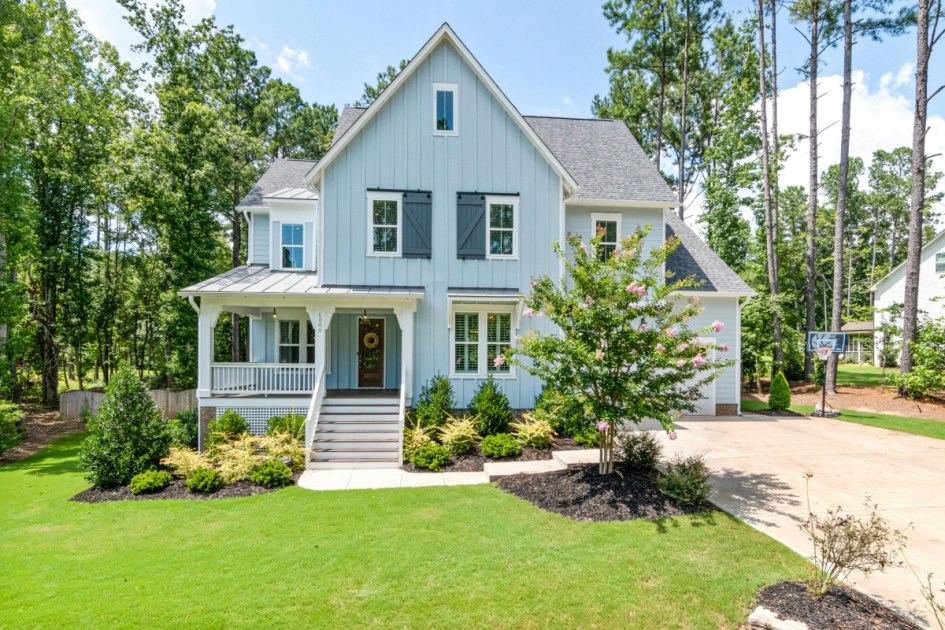 a renovated barn style blue home with shutters, white details, a porch, and a basketball hoop in the driveway