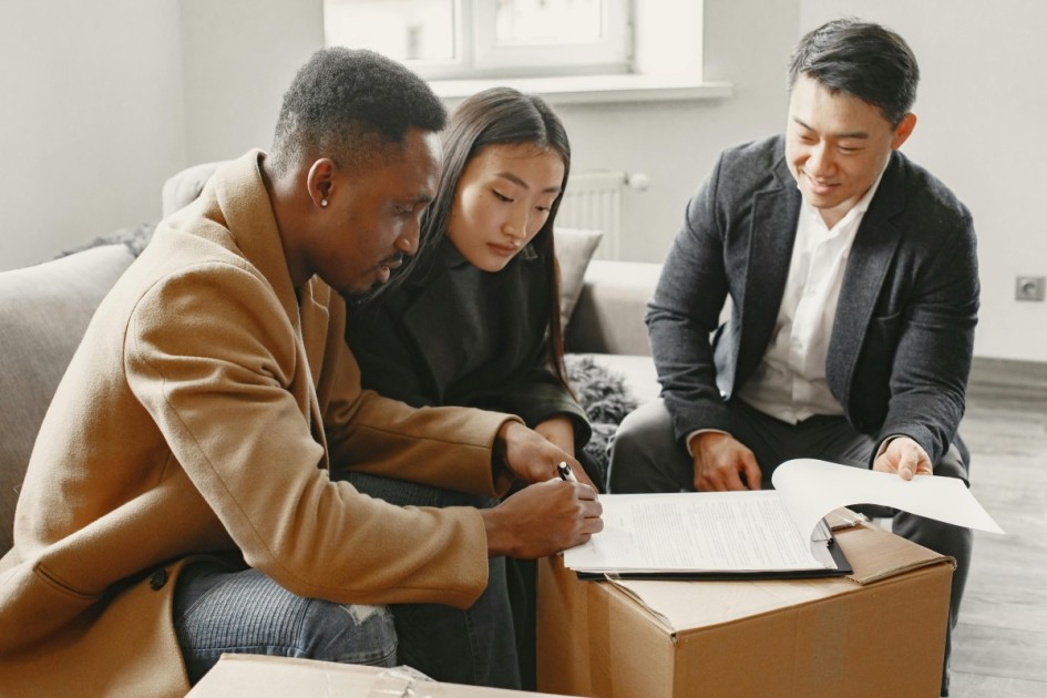 a couple sits on a couch with a real estate agent and signs a new construction home after learning how to negotiate new home price with builder