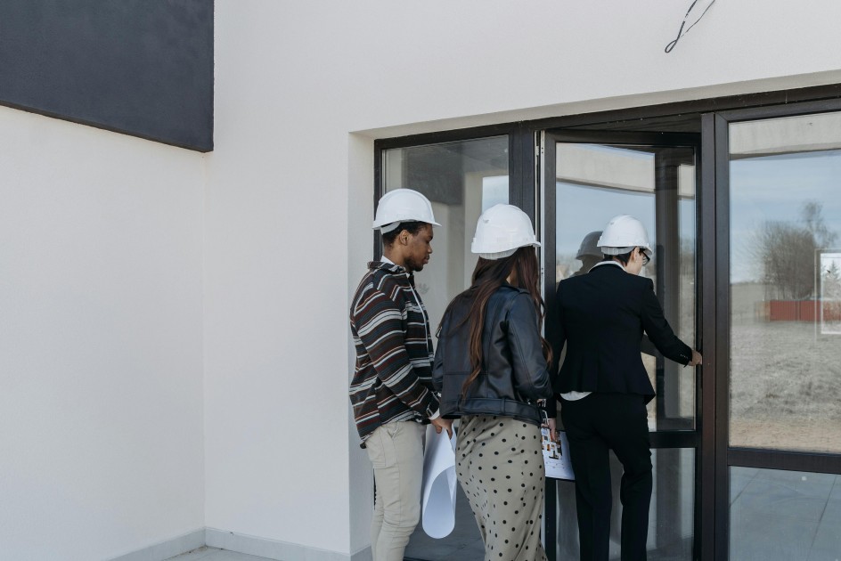 a couple in a hard hat enter a new construction home with a realtor as they decide if it's better to buy a new or existing home