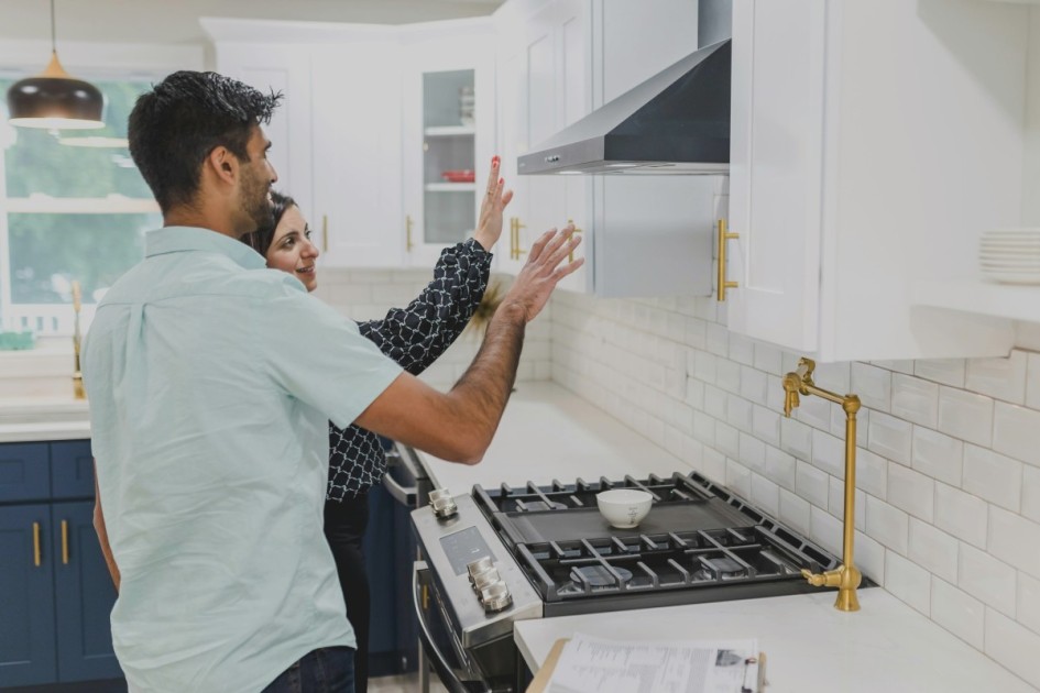 a man and woman inspect a kitchen's white cabinets wondering how to know if a house is overpriced
