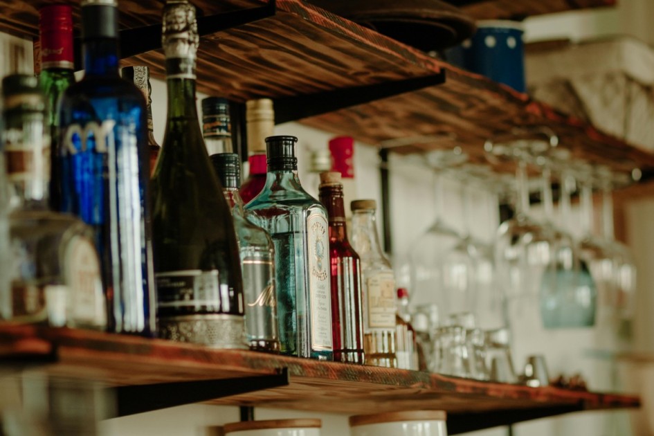 several alcohol bottles and glasses sit on a floating wooden shelf at a home dry bar