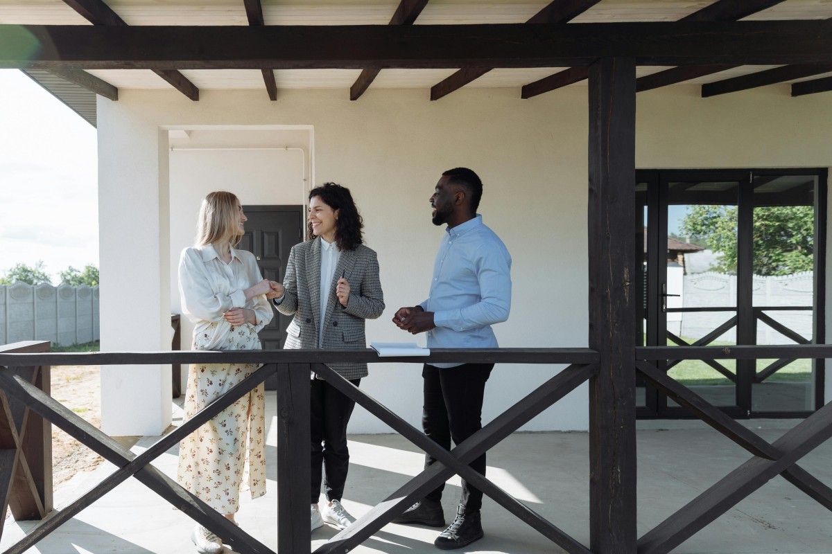 a woman and man talk to a real estate agent on a home's porch