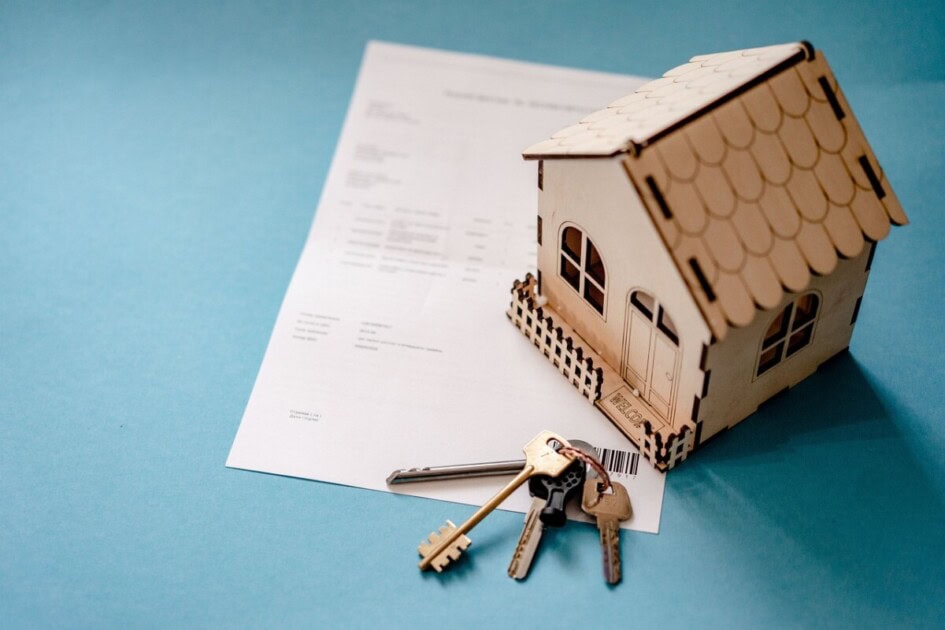 A wooden house and set of keys sit on a mortgage refinance application 