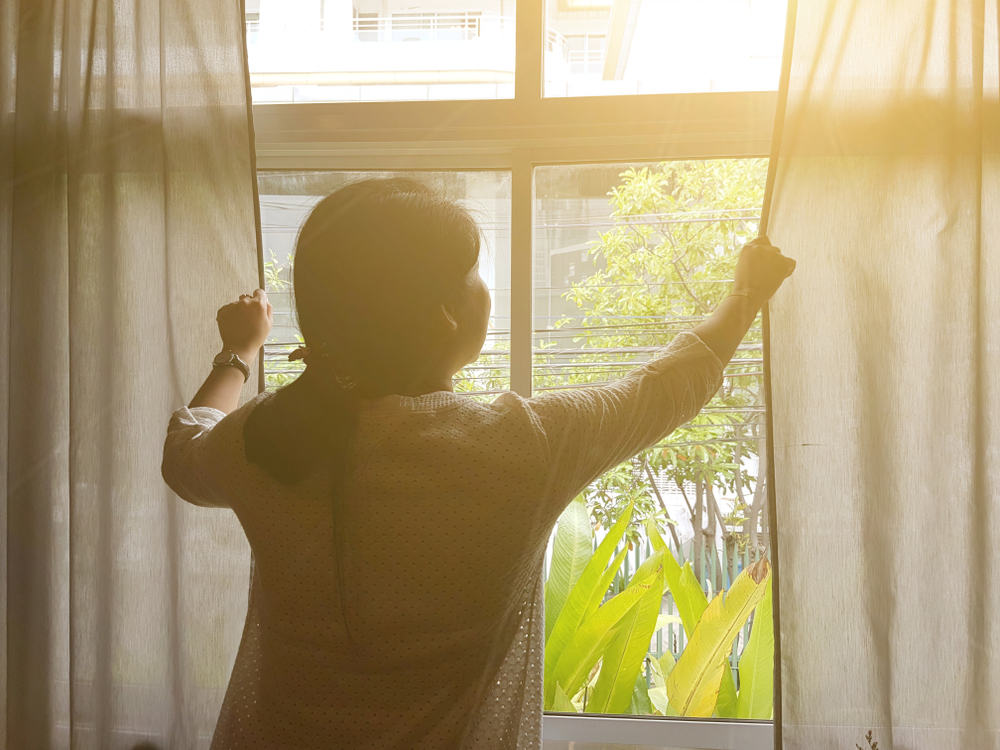 woman pulling curtains closed as the sun shines through