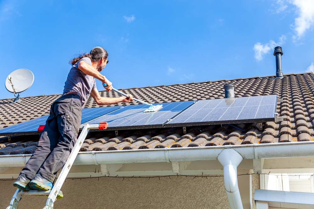 a man on a ladder cleaning solar panels on the roof of a house