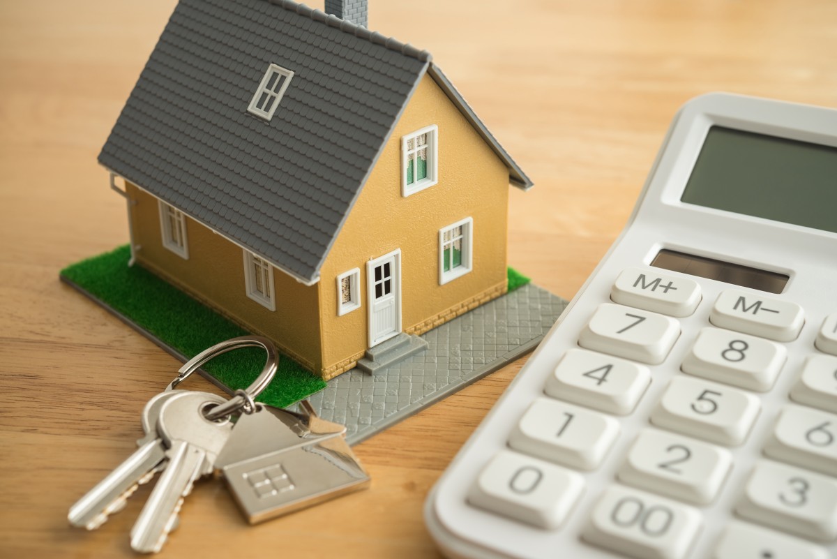 House model, key and white calculator on wooden table background. Mortgage loan for buying home or real estate property, money saving plan, money risk management in financial banking concept.