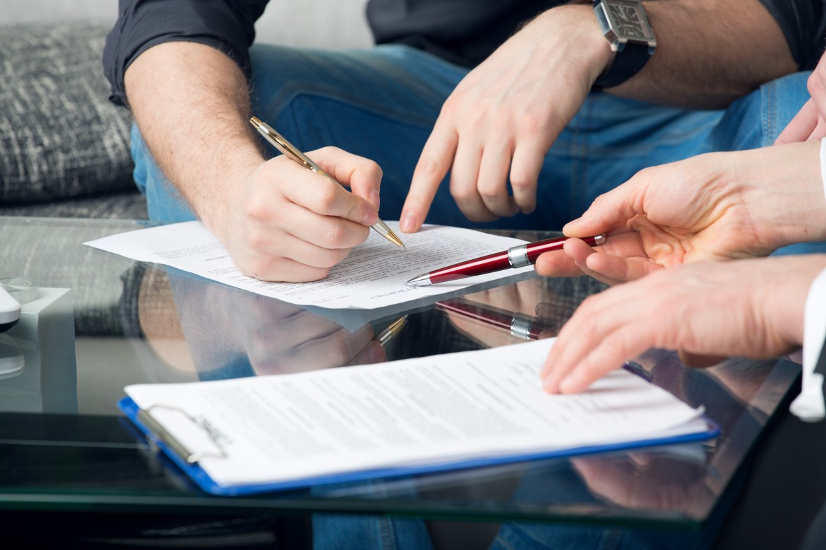 Close up of people's hands signing closing documents on a coffee table.