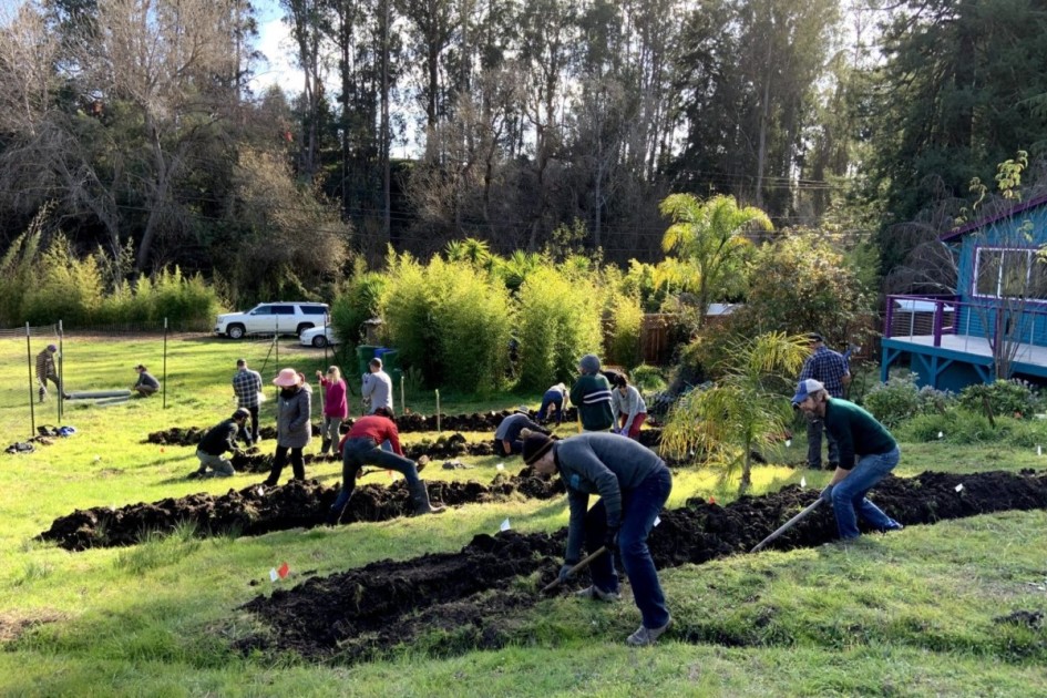 several people work on building a swale-a system for harvesting rainwater-outside a blue home