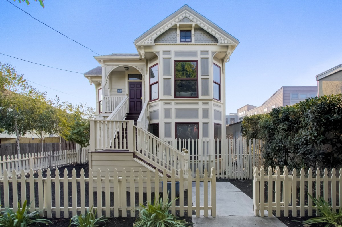 victorian home with light gray exterior and white trim with a blue sky in the background and a white fence